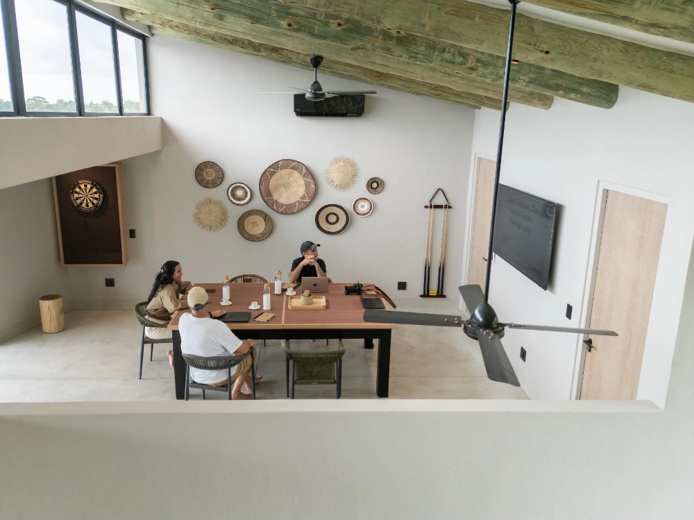Guests sitting around a table in the Izakithi River Villa entertainment room, featuring basket wall décor, a dartboard and a TV.