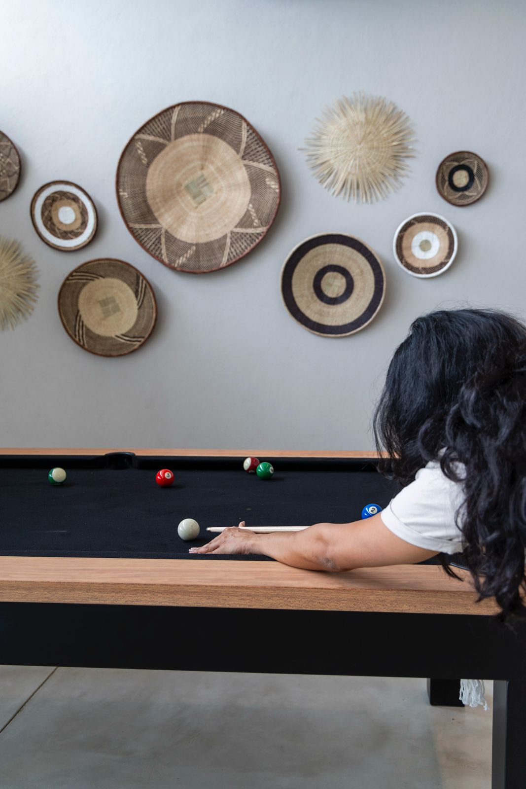 Woman playing pool in a modern lodge, with African wall baskets as decor.